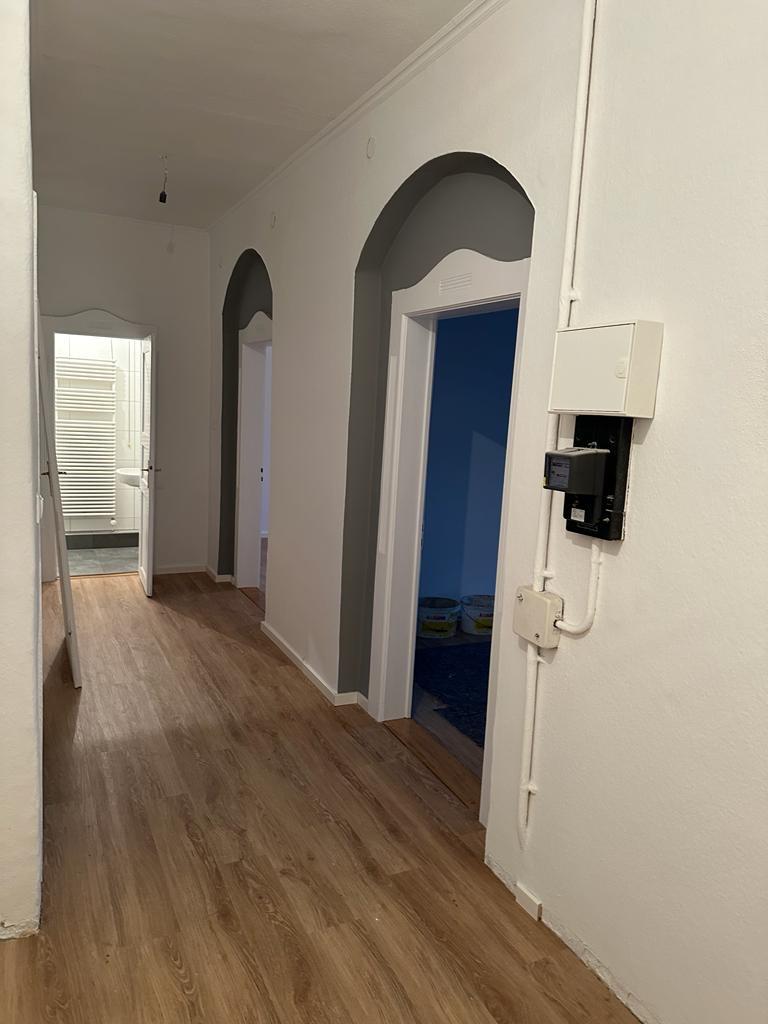 Renovierter Flur mit weiß gestrichenen Wänden und grauen Türbögen – moderner Innenanstrich mit stilvollen Farbkontrasten und neu verlegtem Holzfußboden.