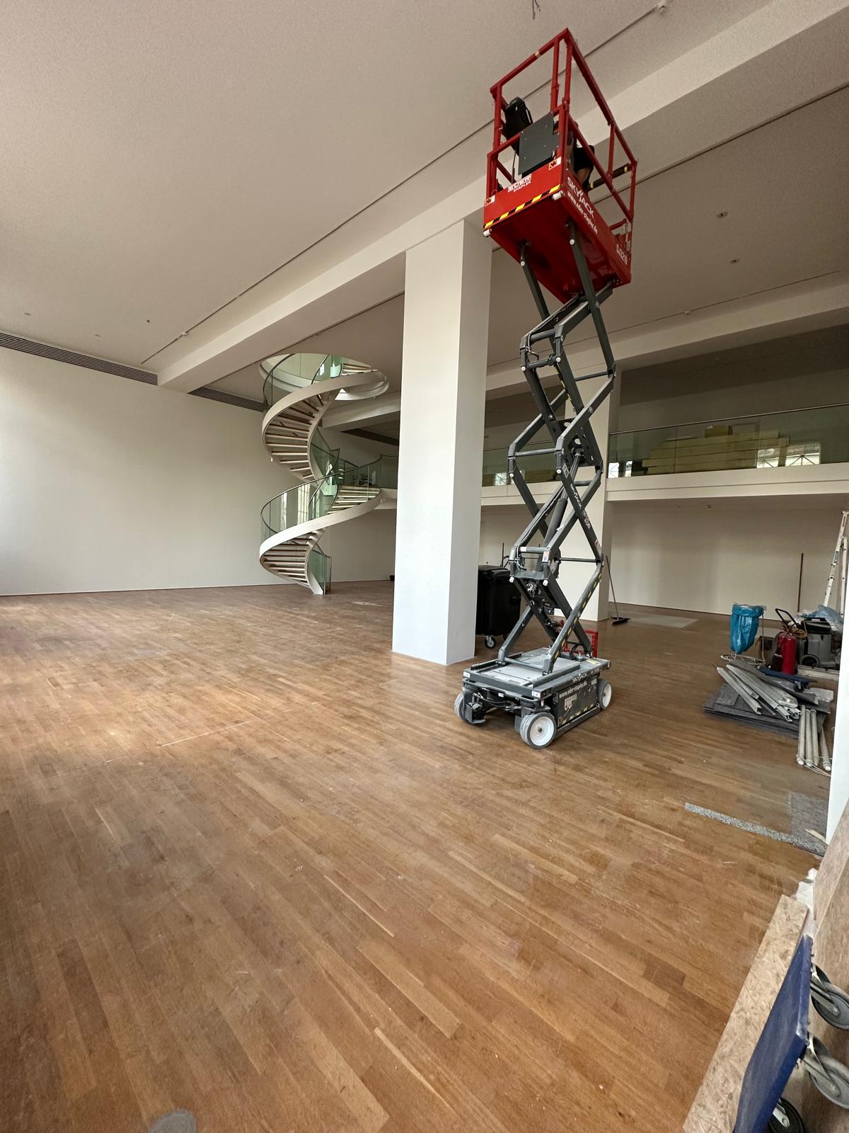 Großer Innenraum mit moderner Wendeltreppe und Hubarbeitsbühne – professionelle Malerarbeiten und Deckenanstrich in großzügigem, lichtdurchflutetem Gebäude.