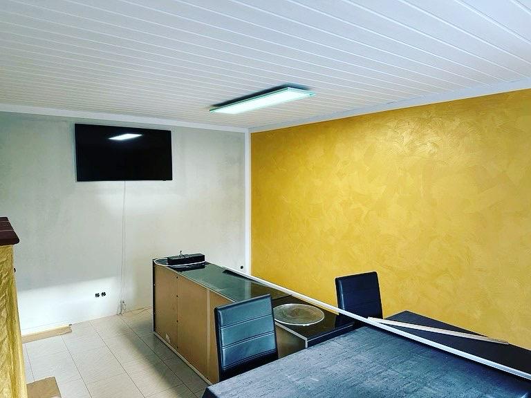 Innenraumgestaltung mit moderner gelber Wischtechnik an der Wand – professionell ausgeführte Malerarbeit in einem Büro mit Schreibtisch, Stühlen und heller Deckenbeleuchtung.